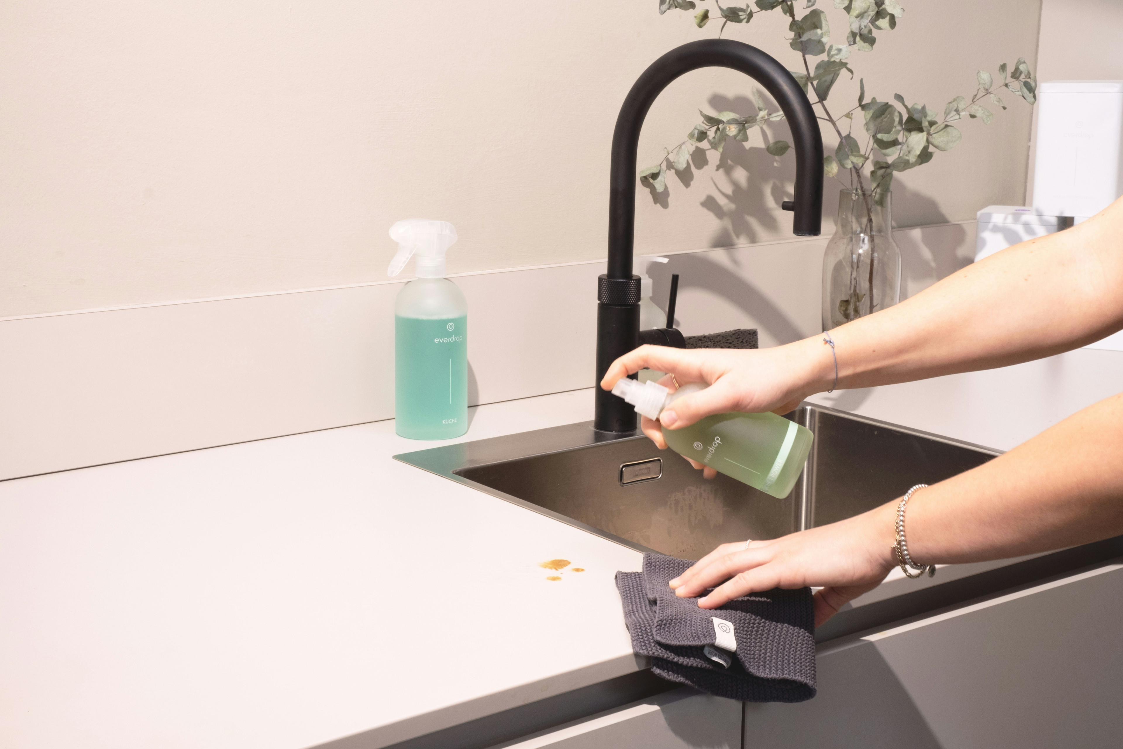 Reinigung einer Küchenarbeitsplatte mit Reinigungsmittel und Tuch an einem modernen Waschbecken