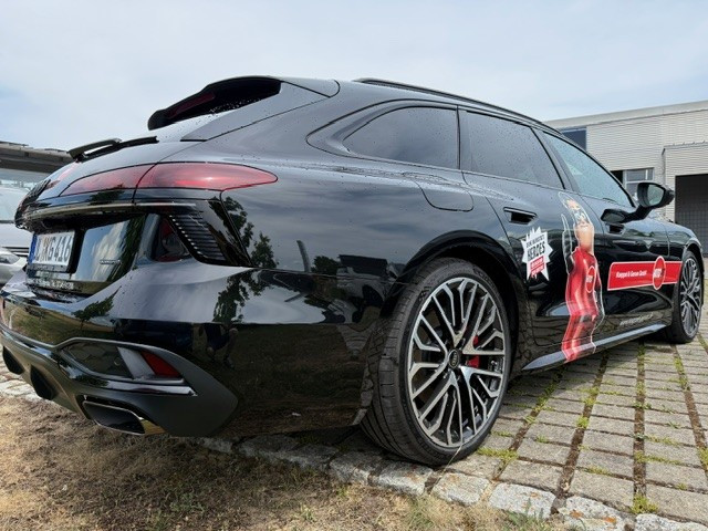 Schwarzer Sportwagen mit auffälligem Felgendesign und Werbebeklebung auf einem Parkplatz