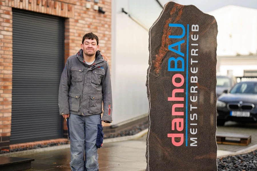 Nico von Haustechnik bei DanhoBau Meisterbetrieb Nico von Haustechnik vor dem DanhoBau Meisterbetrieb Schild