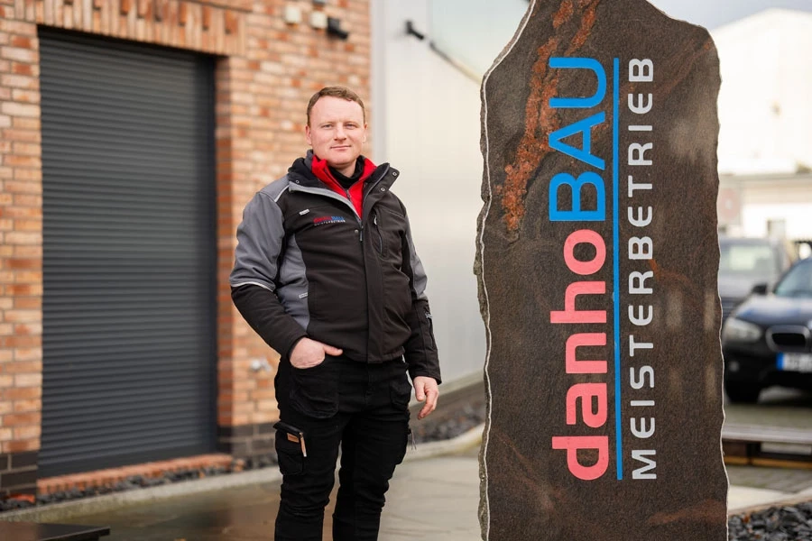 Mariusz P. Schlosser bei Danho Bau Meisterbetrieb Mariusz P. vor einem Gebäude mit Danho Bau Meisterbetrieb Schild