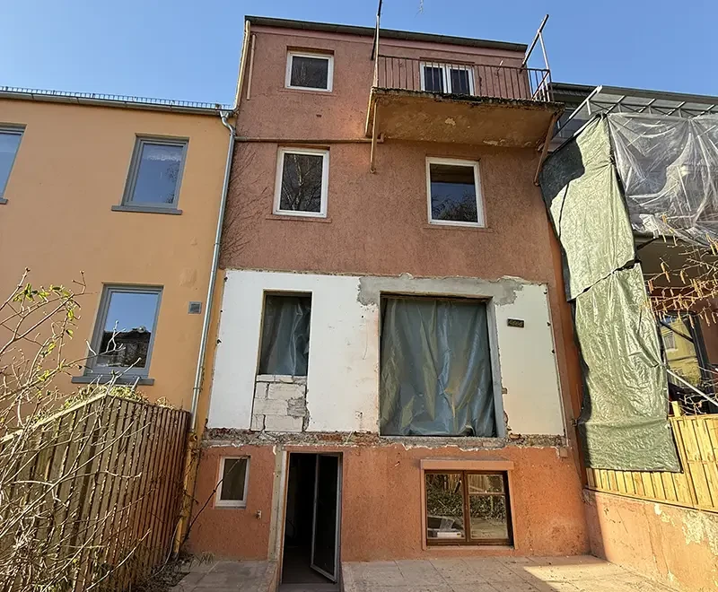 Sanierungsbedürftiges Mehrfamilienhaus mit beschädigter Fassade und Balkon