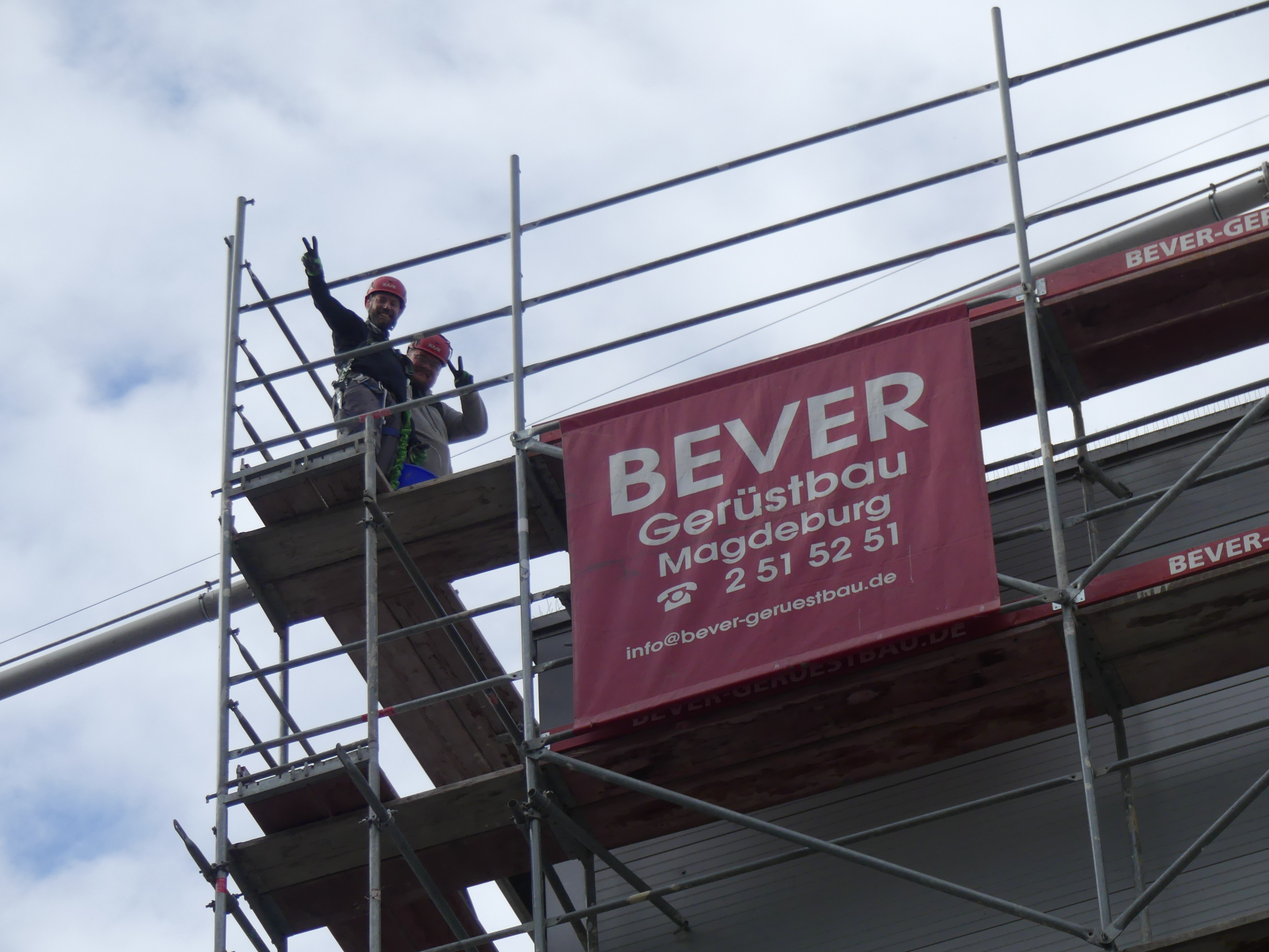BEVER Gerüstbau Magdeburg – Baugerüst mit Bauarbeitern und Werbebanner Baugerüst mit Werbebanner von BEVER Gerüstbau Magdeburg und zwei Bauarbeitern auf dem Gerüst