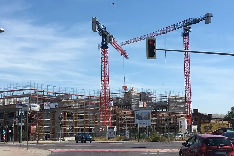 Baustelle mit Arbeits- und Schutzgerüsten – Sicherheit auf dem Bau Baustelle mit Arbeits- und Schutzgerüsten sowie zwei Baukränen unter blauem Himmel