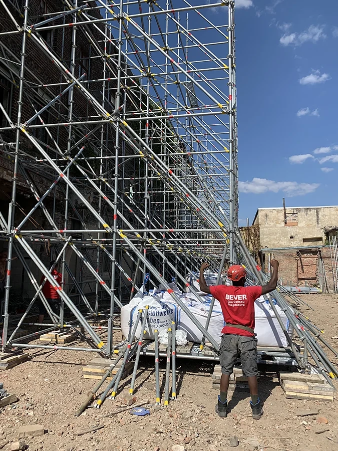 Gerüst auf einer Baustelle mit Bauarbeiter beim Aufbau unter blauem Himmel