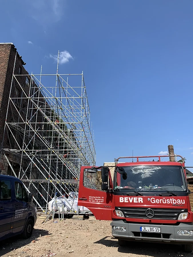 Baustellenwagen von Bever Gerüstbau vor eingerüstetem Gebäude unter blauem Himmel