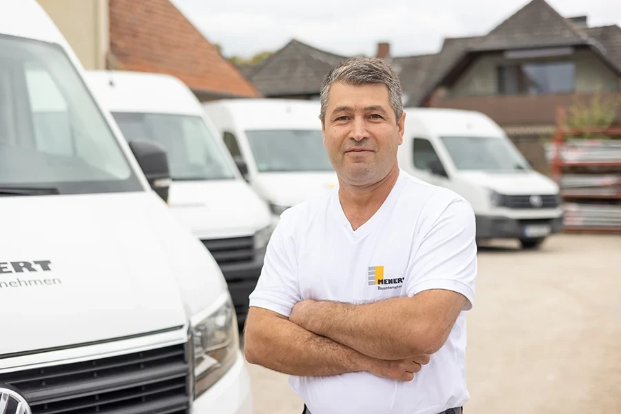 Dogan Alo von Mener Bauunternehmen steht vor weißen Transportern