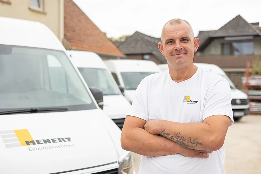 Daniel Lulinski vor Firmenfahrzeugen des Unternehmens Mehnert, mit sichtbarem Tattoo am Arm