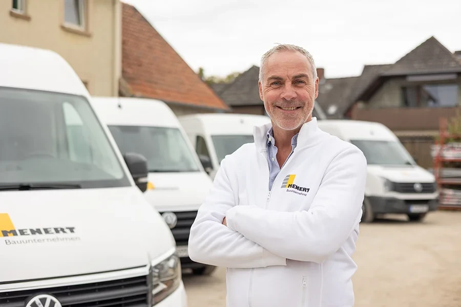 Christian Riedel, Maurermeister bei HENERT Bauunternehmen, steht vor Firmenfahrzeugen