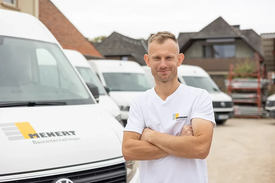 Rafal Stefaniak im Firmen-T-Shirt von Menert Bauunternehmen vor Firmenfahrzeugen