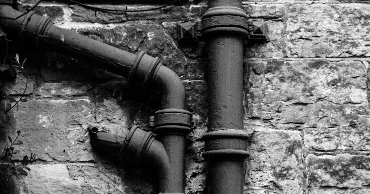 Schwarz-Weiß-Foto von einem Rohr an einer Steinwand