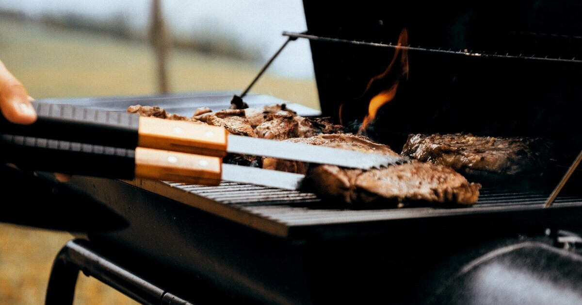 Grillen von Fleisch auf einem Holzkohlegrill mit Grillzange und Flamme