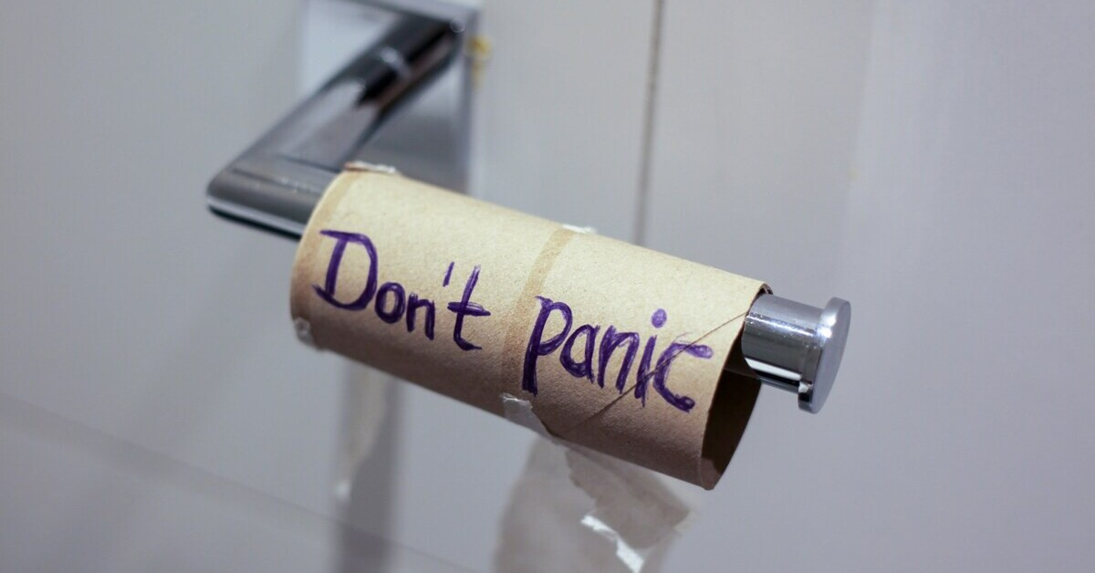 Leere Toilettenpapierrolle mit Aufschrift 'Don't panic' auf der Toilette
