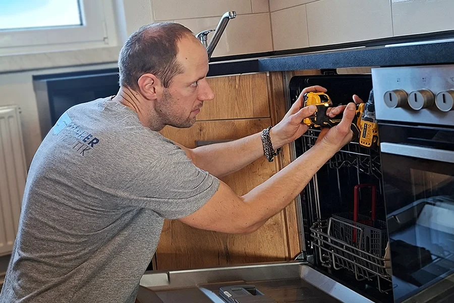 Küchenmontage: Handwerker montiert Geschirrspüler in moderner Küche