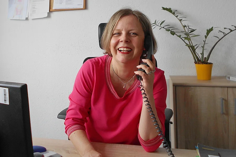 Franziska Janke am Schreibtisch im Büro, telefonierend, mit pinkem Pullover
