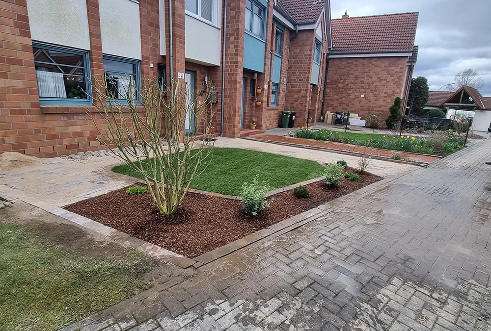Moderner Vorgarten mit Rasenfläche und gepflegten Beeten vor einem Reihenhaus