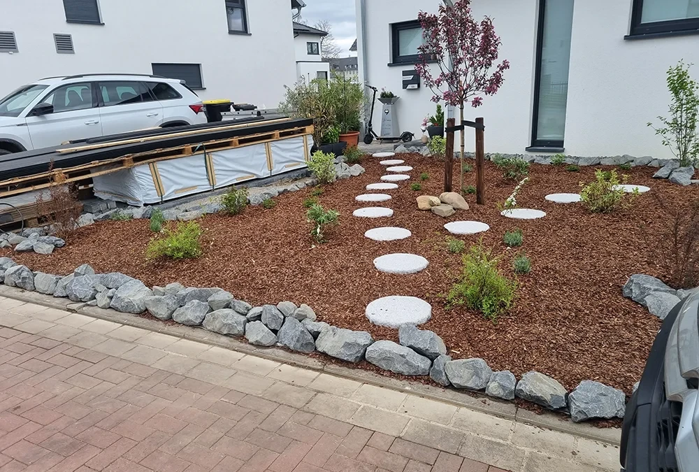 Moderner Vorgarten mit Rindenmulch, Steinen und Trittplatten vor einem Einfamilienhaus