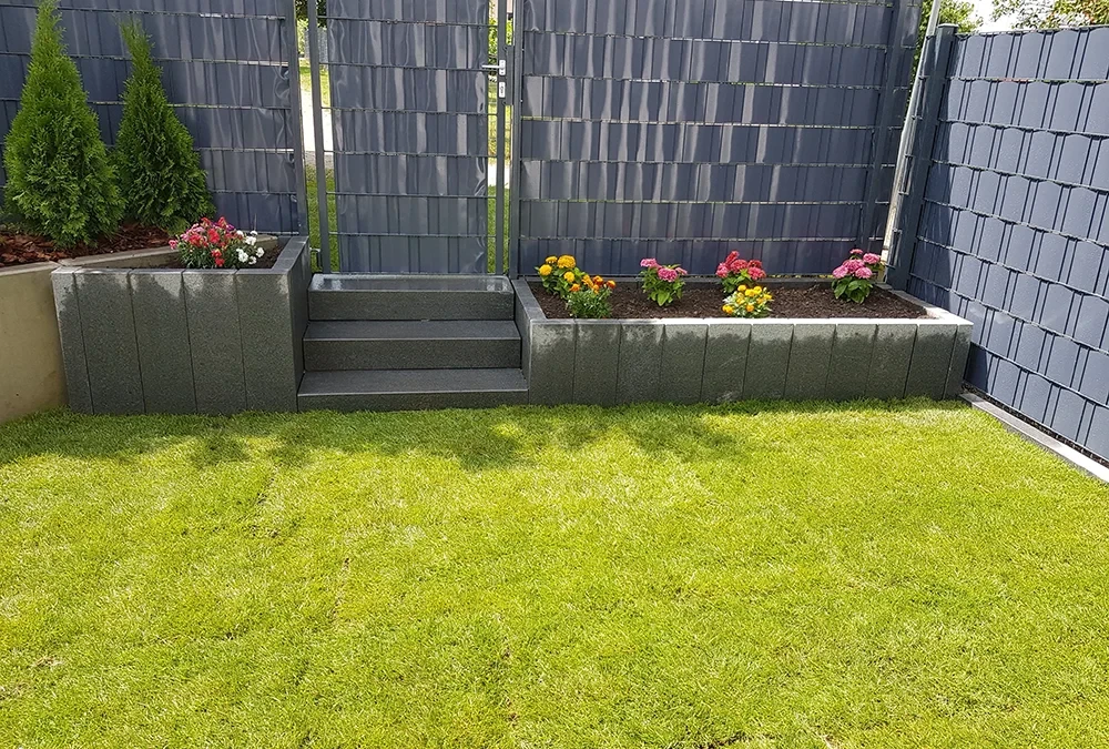 Moderner Garten mit grünem Rasen, Sichtschutzzaun und bepflanzten Hochbeeten