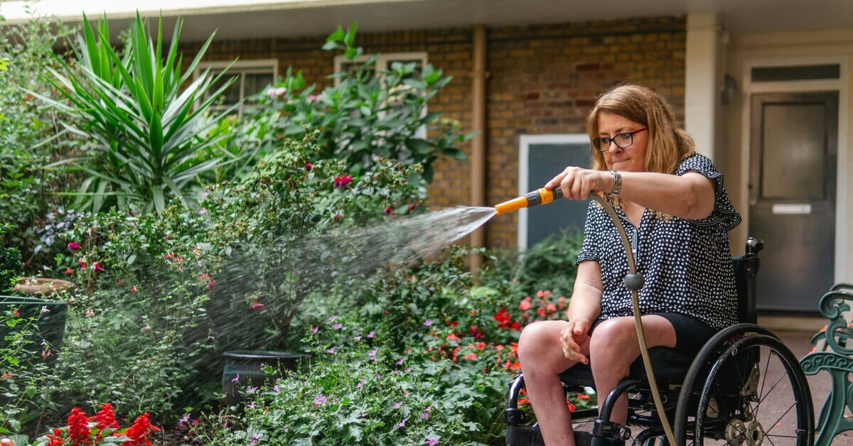 Frau im Rollstuhl gießt den Garten mit einem Wasserschlauch