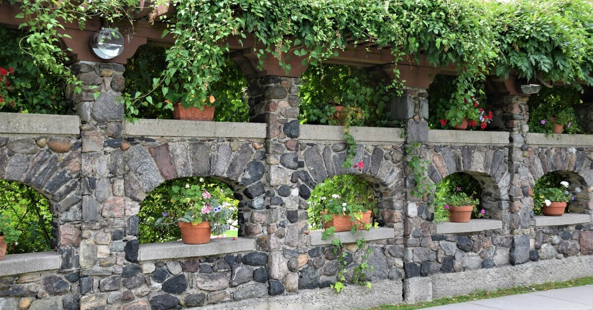 Naturstein-Gartenmauer mit bepflanzten Töpfen und Rankpflanzen im Garten