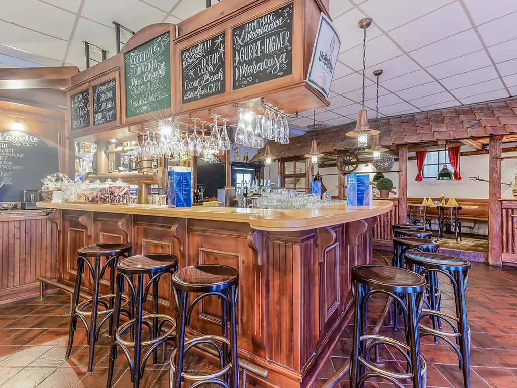 Gemütliche Bar mit Holztresen und Barhockern in einem Restaurant, verschiedene Cocktails und Limonaden auf Tafeln angeboten