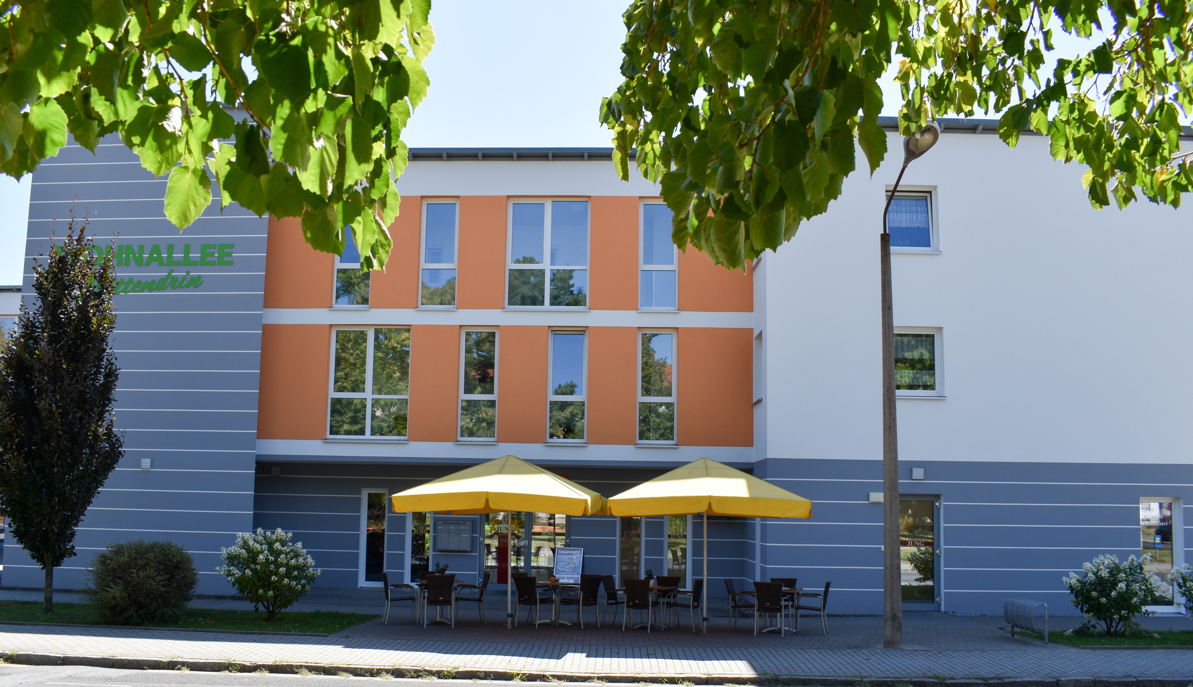 Modernes Wohnhaus mit Straßencafé und gelben Sonnenschirmen an einem sonnigen Tag