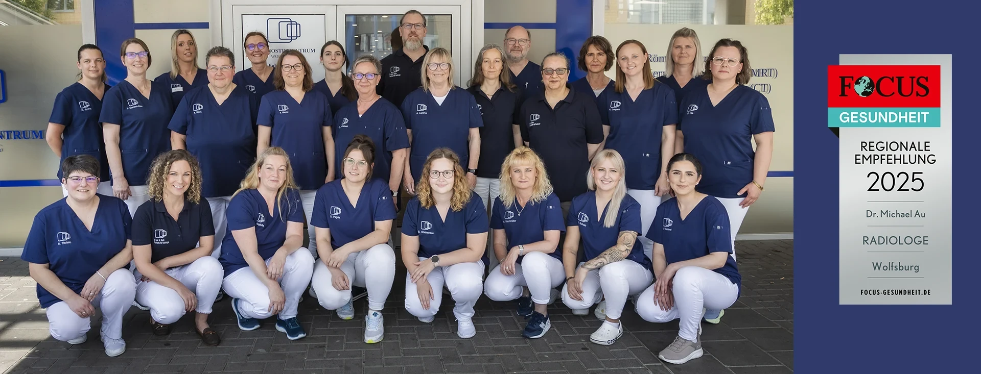 Teamfoto medizinisches Fachpersonal in blauer und weißer Arbeitskleidung vor dem Eingang einer Praxis oder Klinik