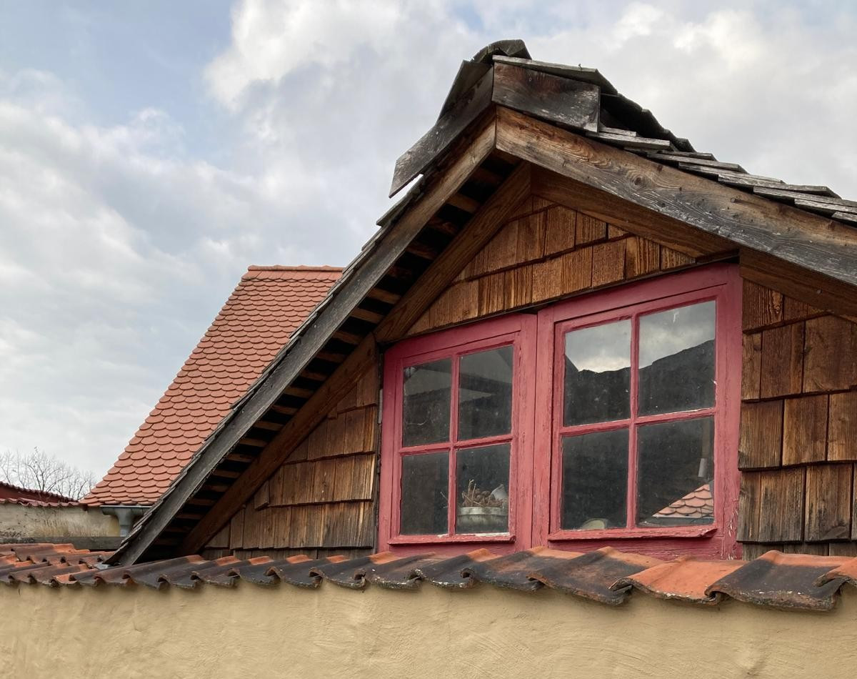 Detailansicht eines alten Mauerdachs mit Fassade und roten Holzfenstern