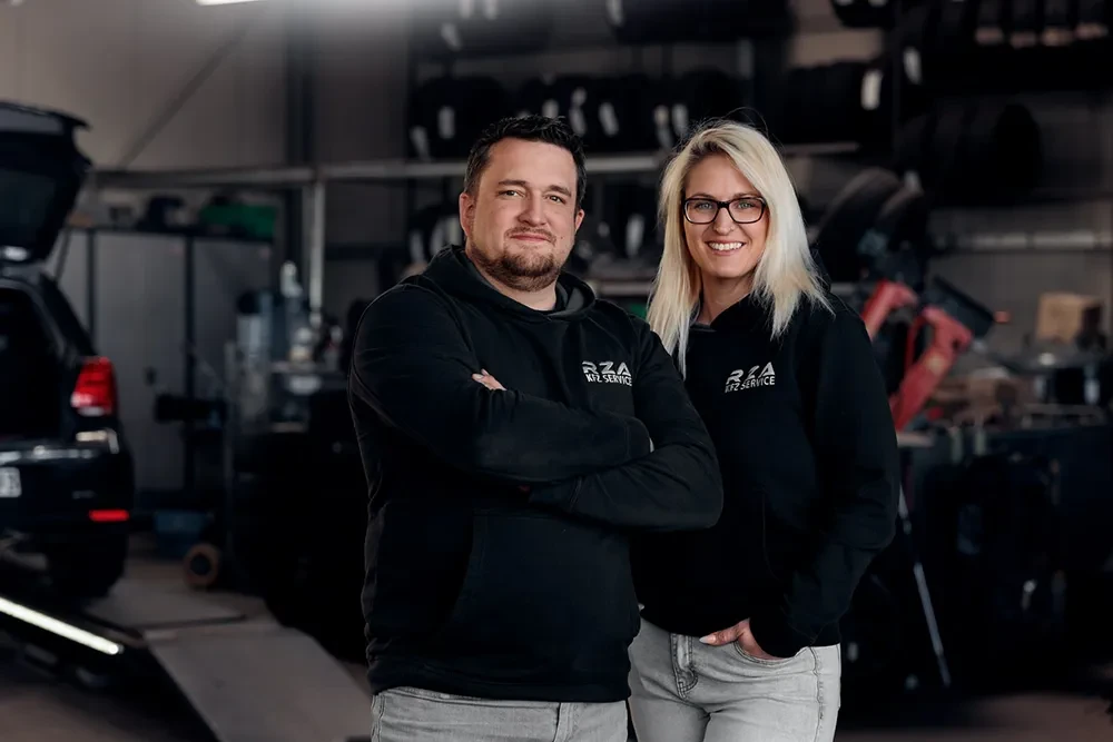 Timo und Michaela Schuhart in der Werkstatt, beide tragen schwarze Hoodies mit RZA KFZ Service Logo