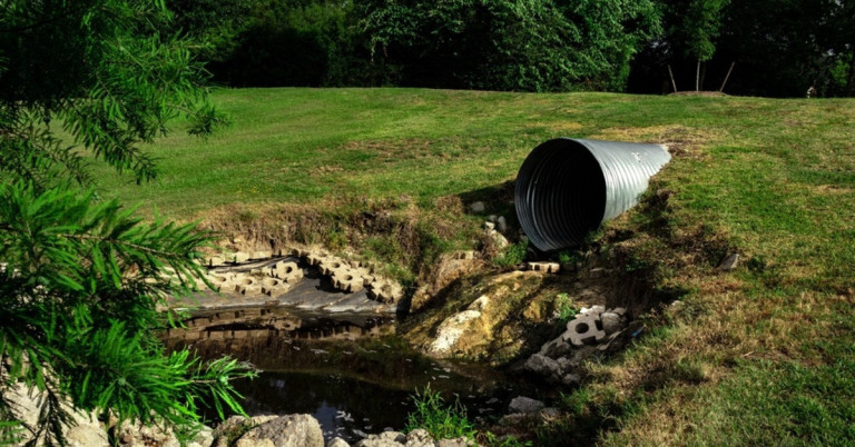 Großes Rohr als Wasserablauf in einer natürlichen Umgebung Großes Rohr in einer grünen Landschaft mit Wasserablauf