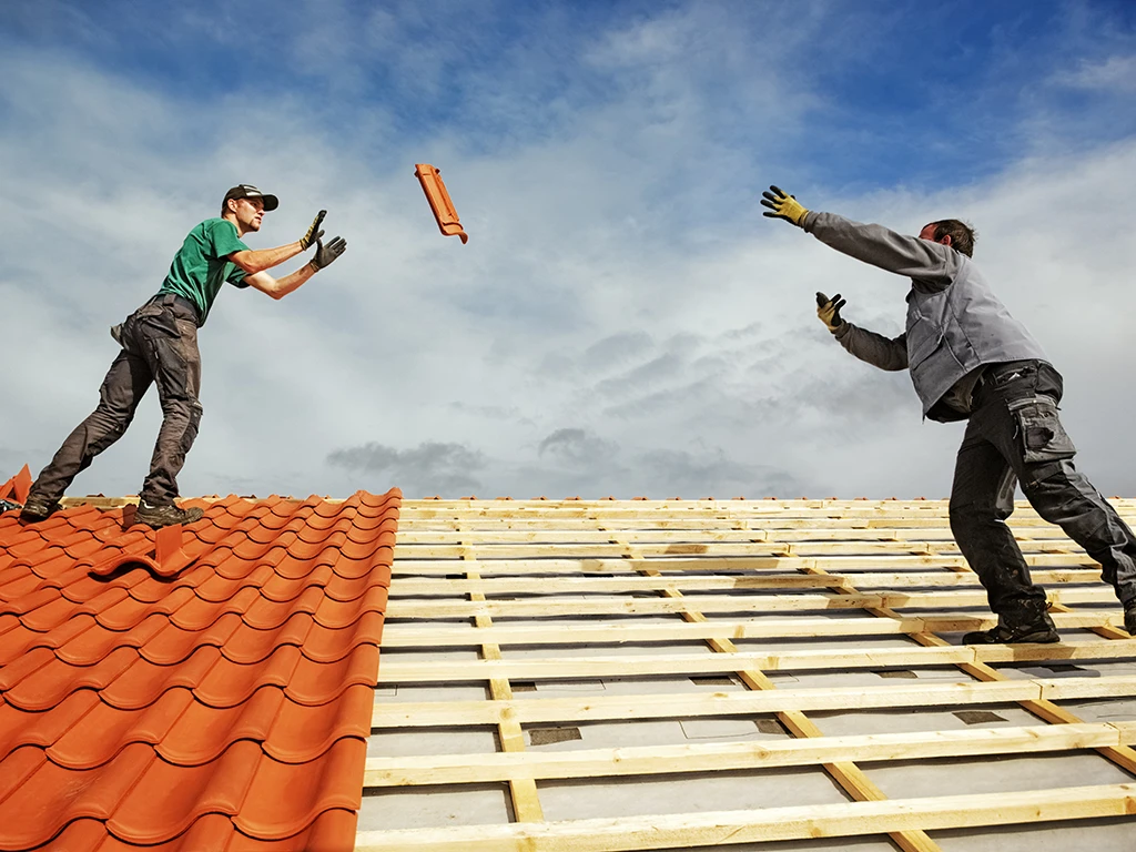 Dachdecker bei der Arbeit auf einem Dach, Dachziegel werden zugeworfen