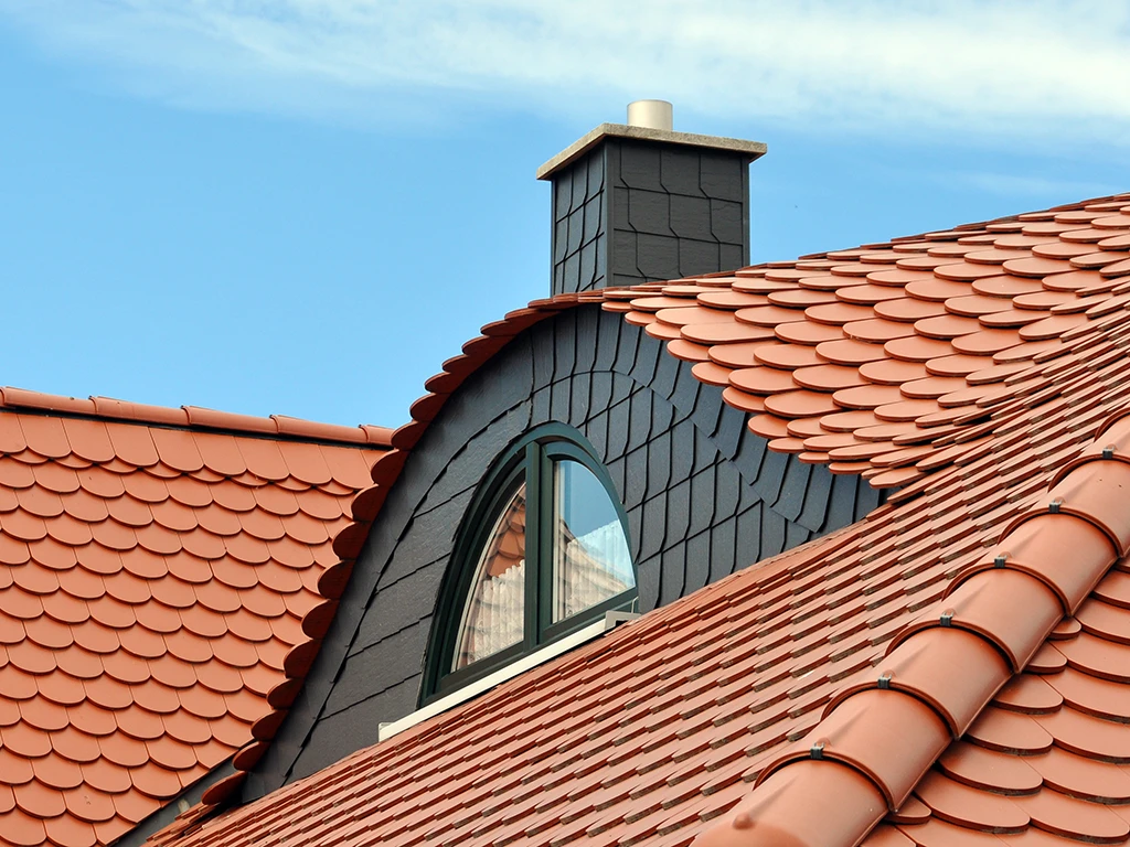 Moderne Dachgaube mit Schieferverkleidung und Ziegeldach unter blauem Himmel