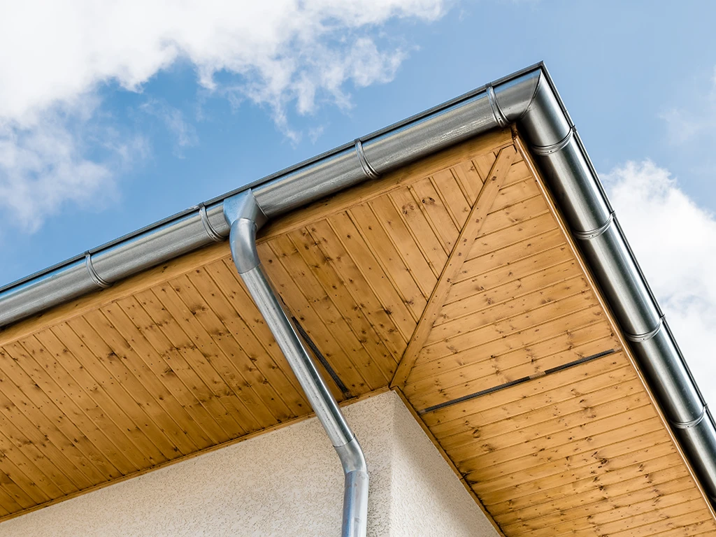 Dachrinne und Fallrohr an einem Haus mit Holzuntersicht bei blauem Himmel