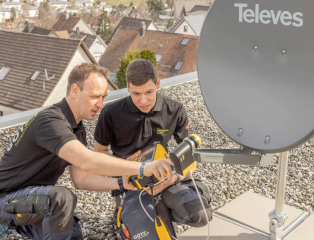 Zwei Techniker richten eine Satellitenschüssel auf einem Hausdach aus
