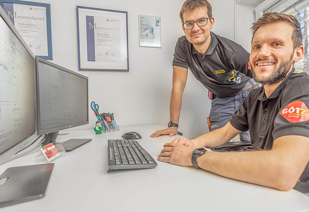Zwei Elektriker im Büro bei der Planung am Computer, Meisterbrief an der Wand