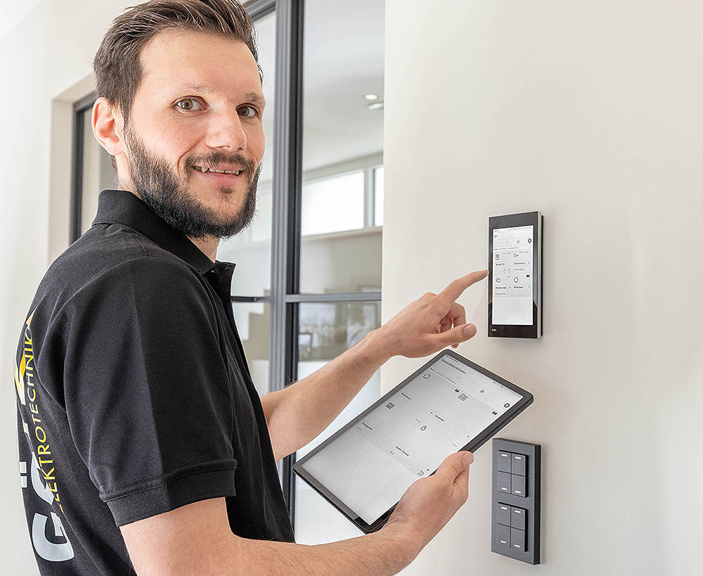Mann bedient Smart-Home-Steuerung an der Wand mit Tablet in moderner Wohnung