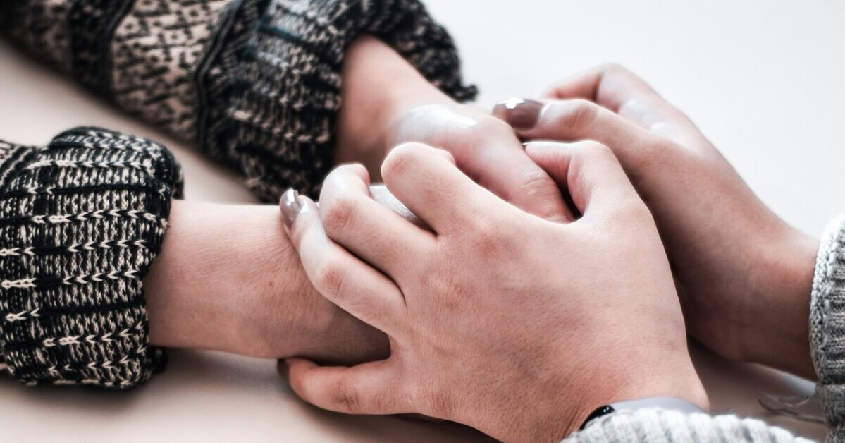 Zwei Hände halten sich auf einer Tischfläche als Zeichen von Unterstützung und Zusammenhalt