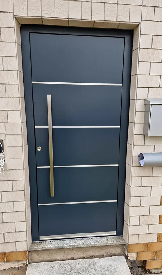 Moderne Haustür aus Metall mit langem Griff und Briefkasten an einer Klinkerfassade