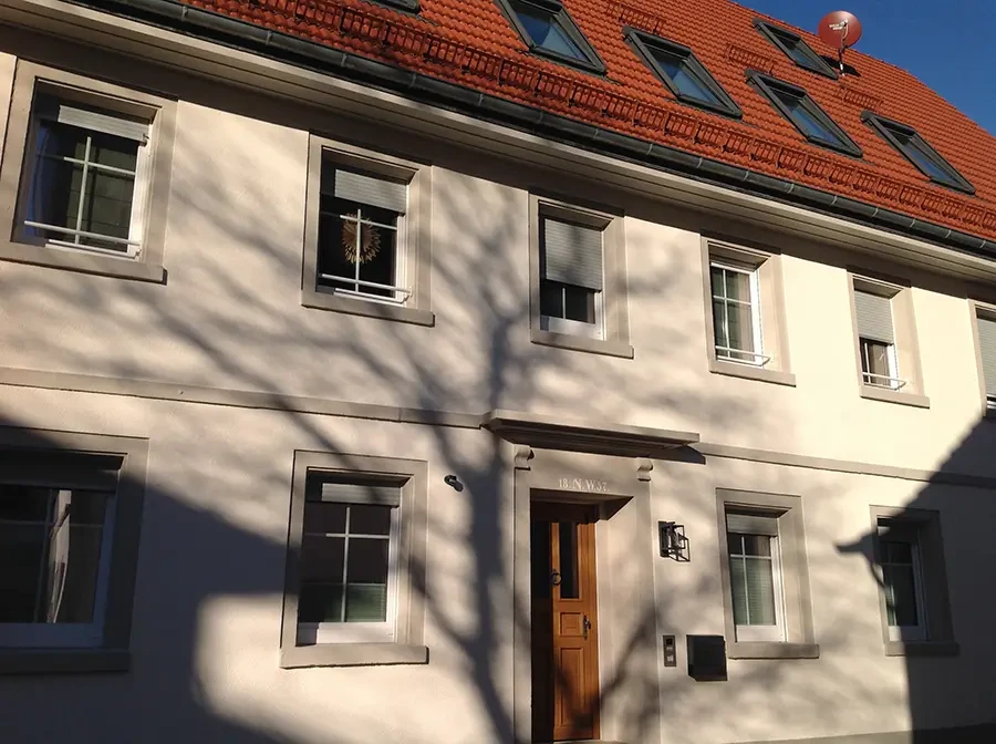 Hauptbild eines Wohnhauses mit weißer Fassade und rotem Dach, Sonnenlicht und Schatten eines Baumes auf der Hauswand