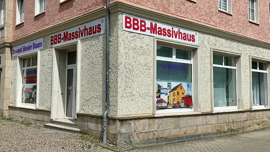 Außenansicht des BBB-Massivhaus Firmengebäudes mit Werbeschild und Schaufenster