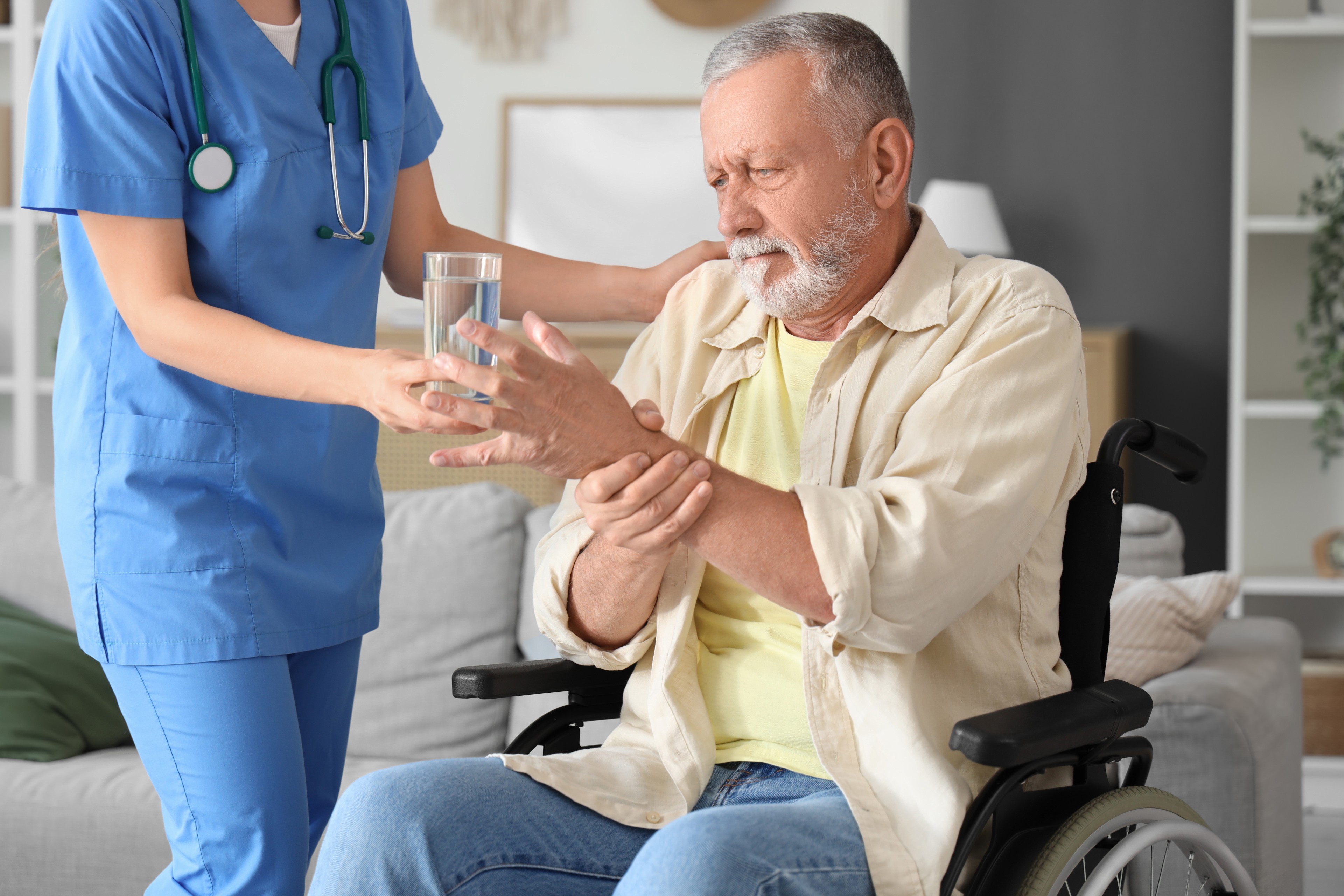 Pflegekraft reicht einem Senior im Rollstuhl ein Glas Wasser