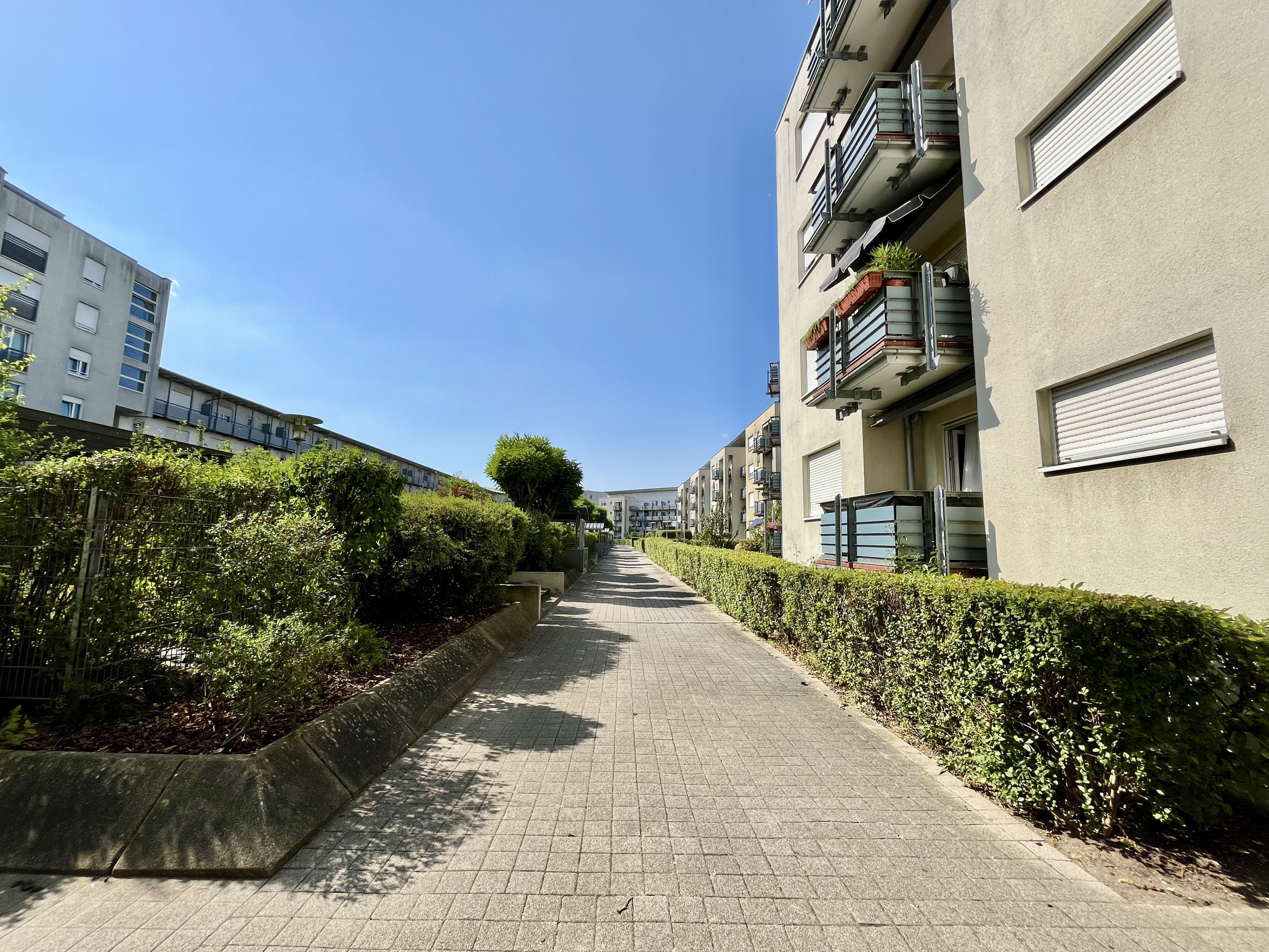 Moderner Wohnkomplex mit Balkonen und gepflegtem Fußweg an einem sonnigen Tag