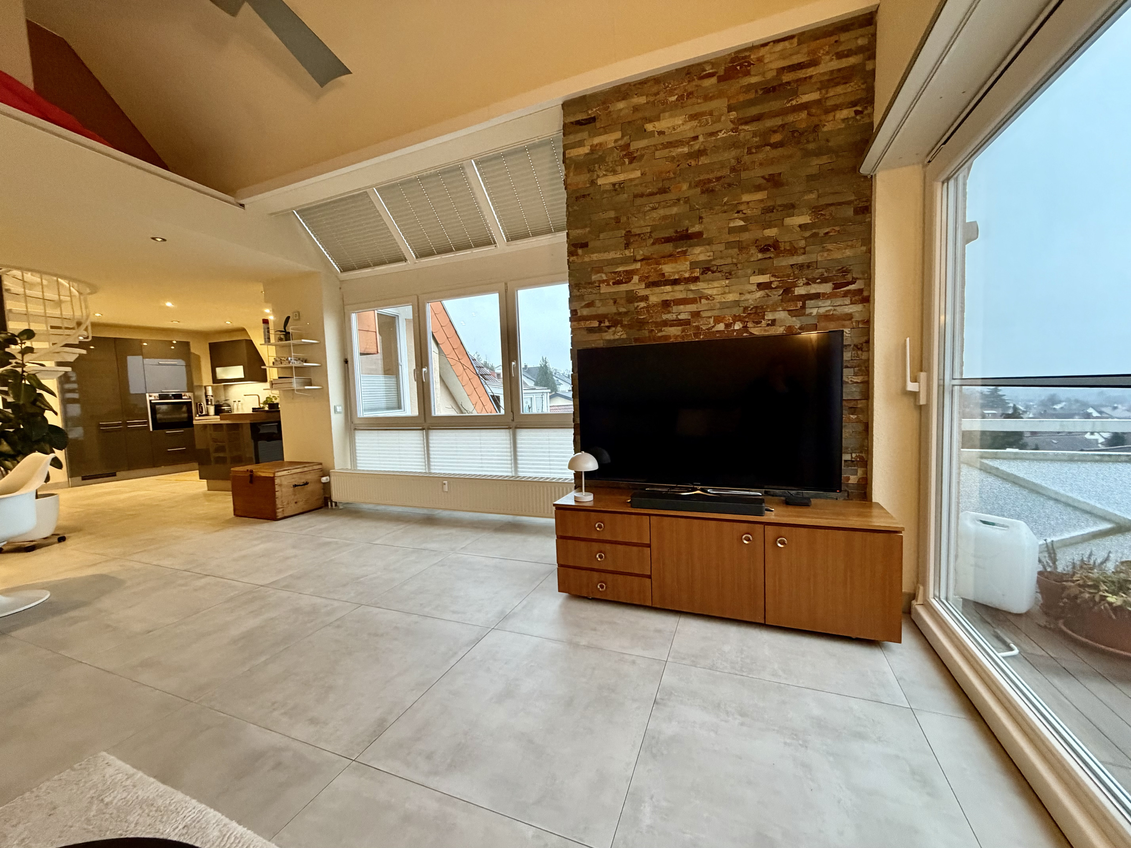 Modernes Wohnzimmer mit großer Fensterfront, Natursteinwand und TV auf Holzkommode