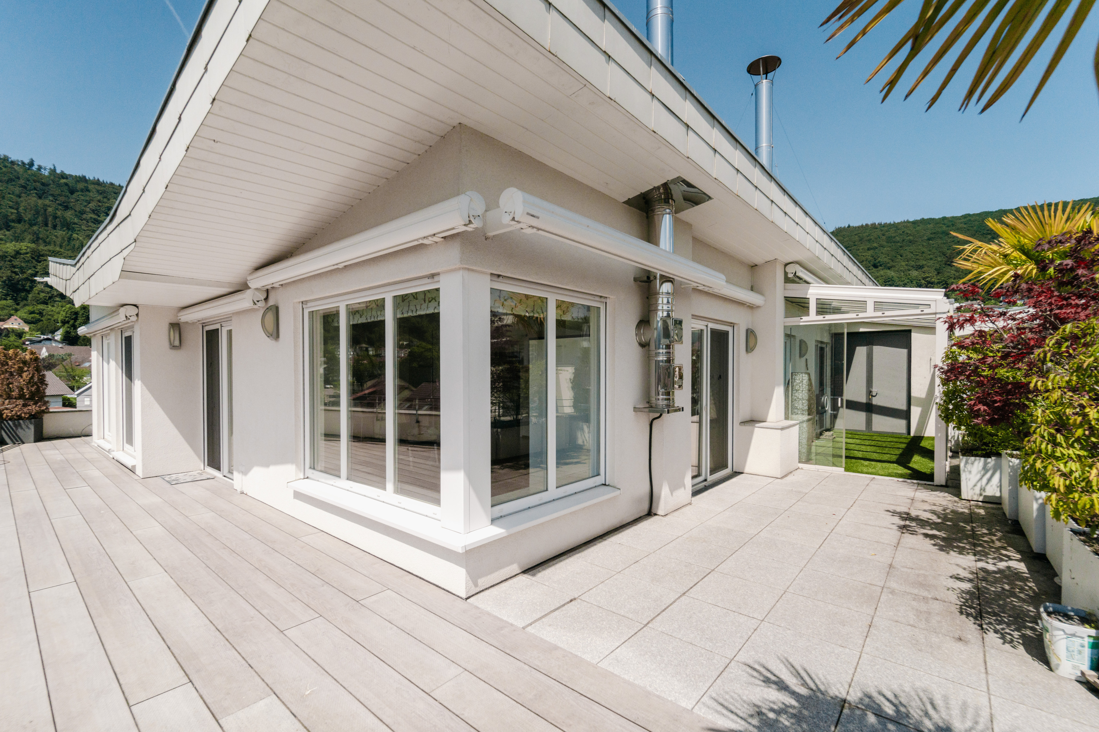 Moderne Terrasse und Hausfassade mit großen Fenstern und Sonnenschutz