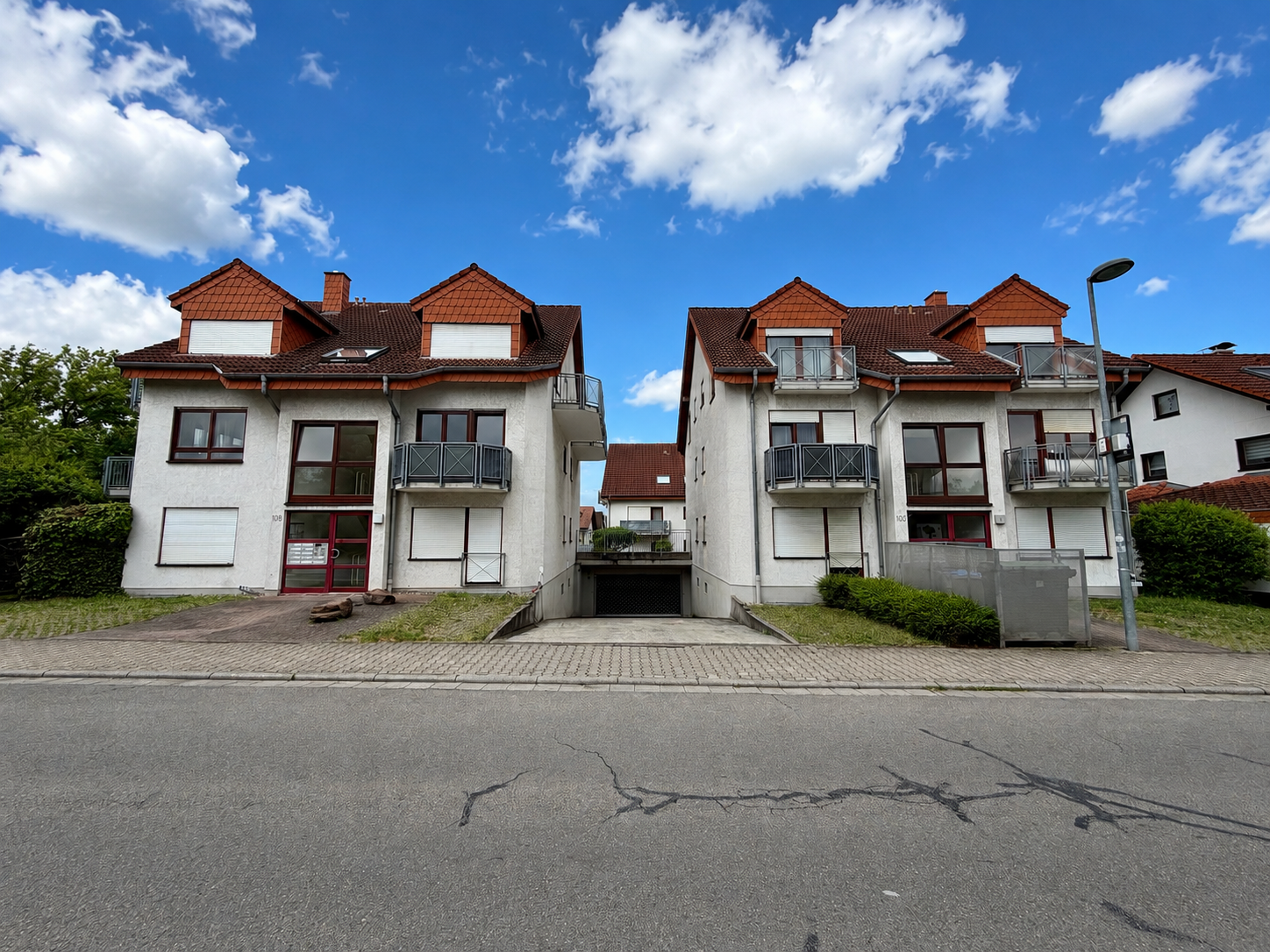 Mehrfamilienhaus mit Tiefgarageneinfahrt und roten Dächern unter blauem Himmel