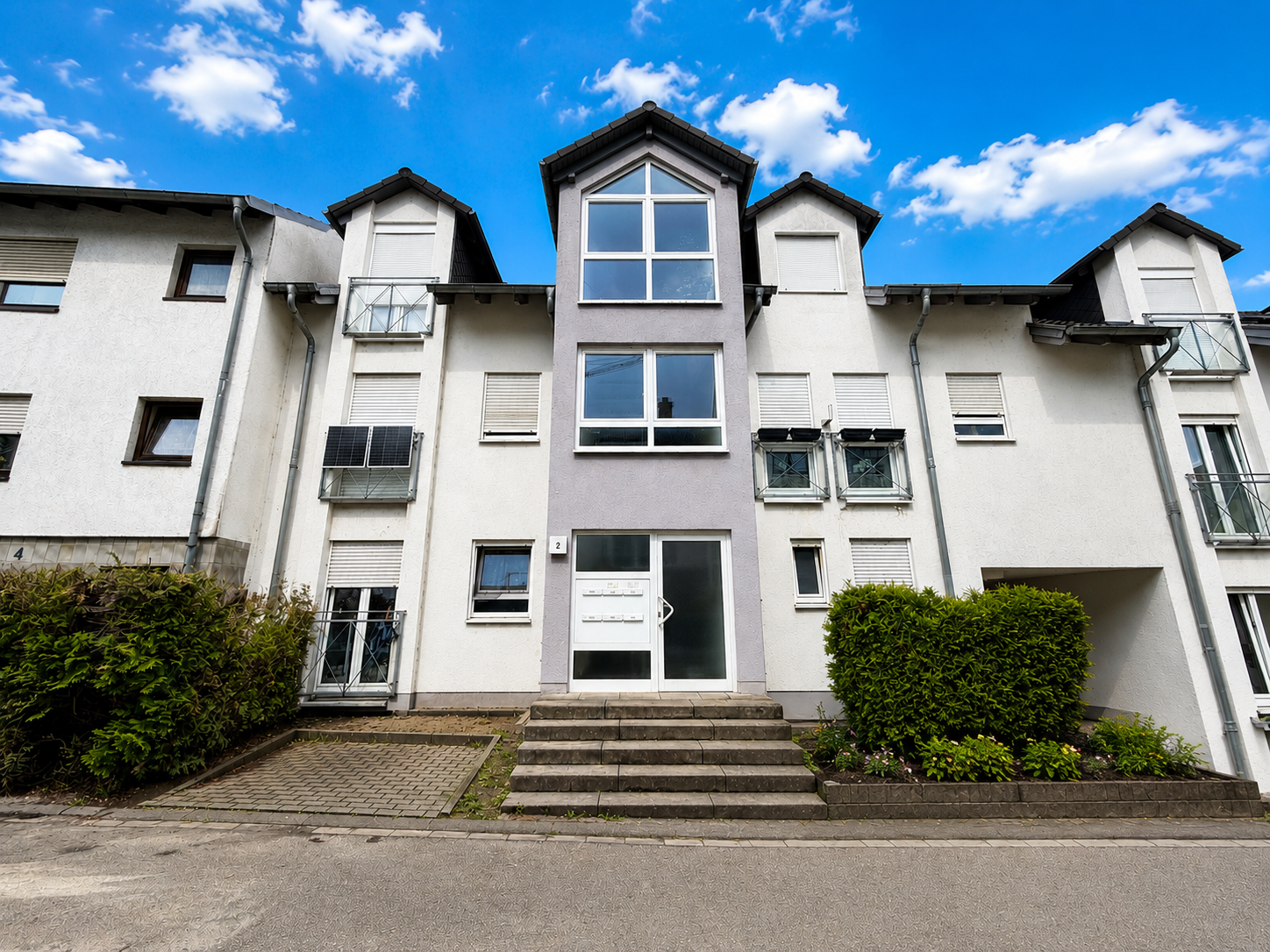 Mehrfamilienhaus mit moderner Fassade und Eingangsbereich unter blauem Himmel