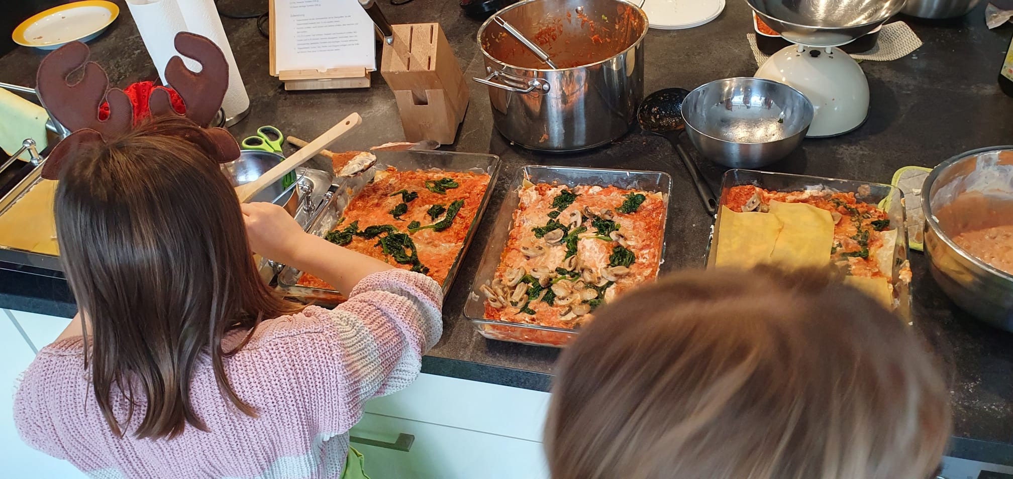 Kinder bereiten gemeinsam frische Lasagne mit Spinat und Champignons in der Küche zu, 7. Dezember 2025.