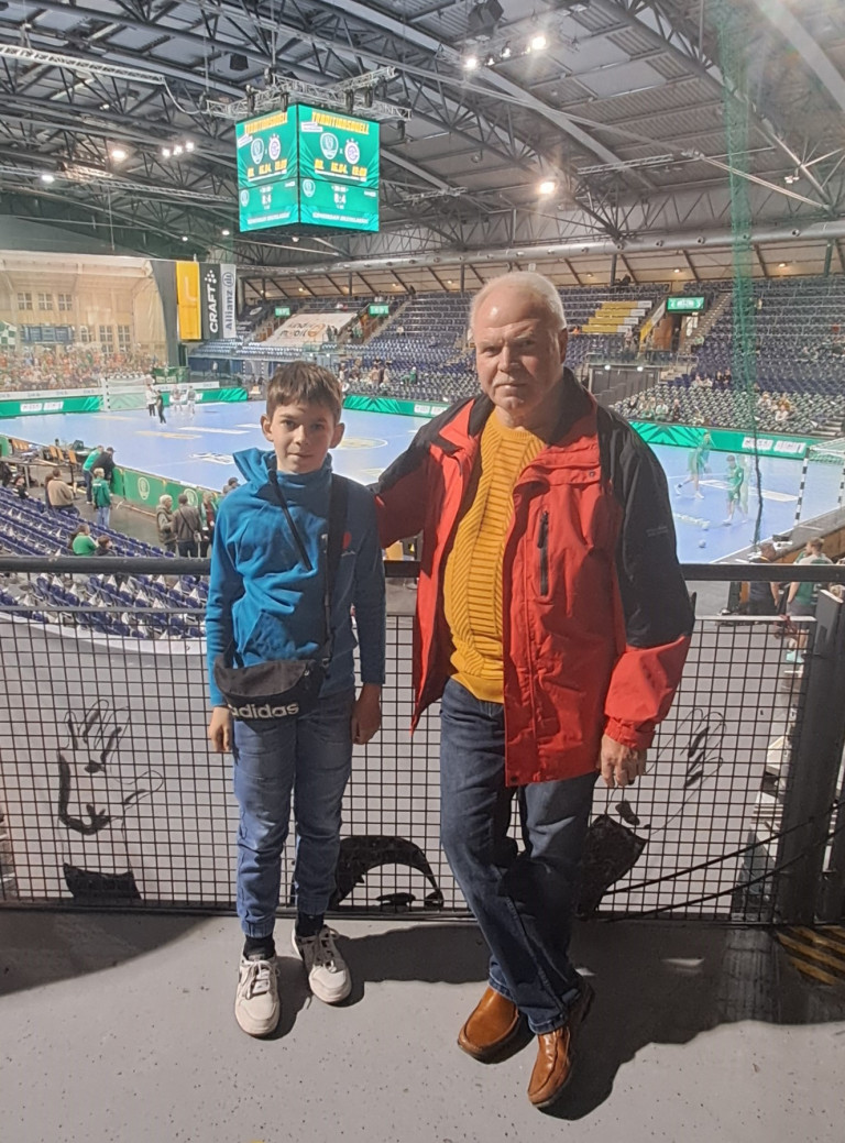 Zwei Personen in einer Handballarena am 09.04.2026, im Hintergrund ein laufendes Handballspiel