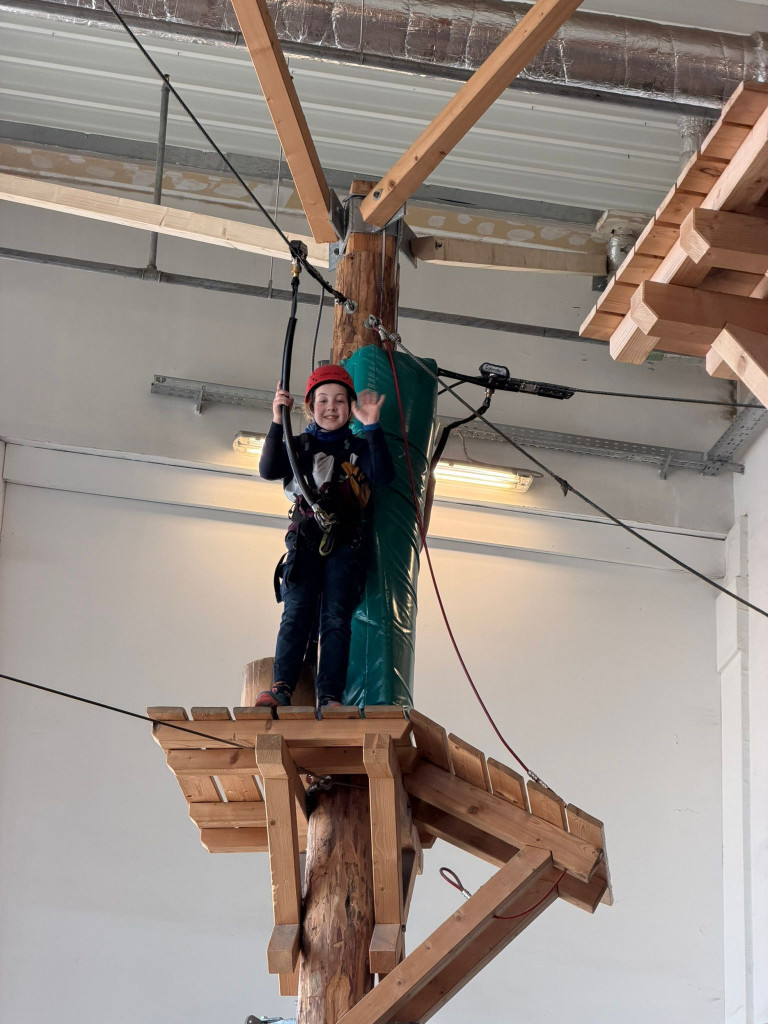 Kind mit Kletterausrüstung im Indoor-Kletterpark auf einer Plattform