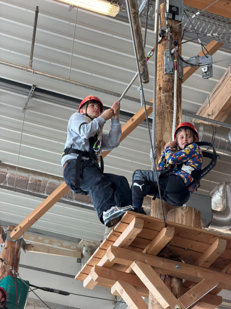 Kinder mit Sicherheitsausrüstung im Indoor-Kletterpark auf einem Parcours
