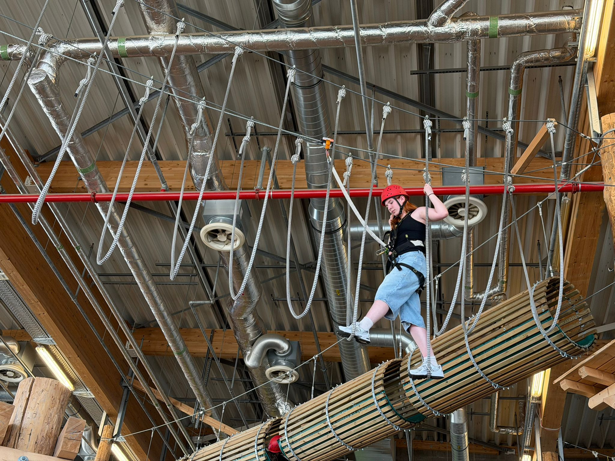 Person im Indoor-Kletterpark auf einem Hochseilparcours mit Sicherheitsausrüstung